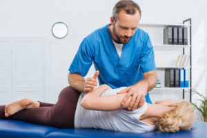 partial view of physiotherapist stretching patient on massage table