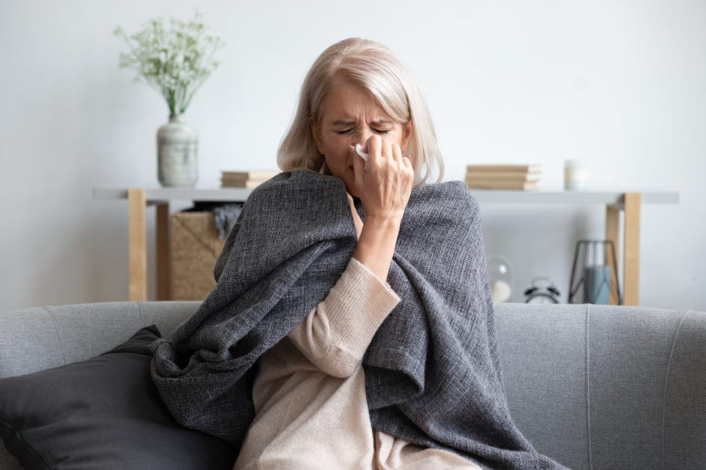 Aged sick woman sneezing holding napkin blow out runny nose