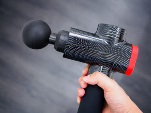 Hand holding a therapeutic massage gun isolated against a dark b